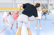 © Westend61 - Instructor with hand on hip doing exercise with students at school sports court