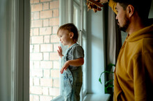 Cute Boy Looking Through Window With Father Holding Airplane Toy At Home