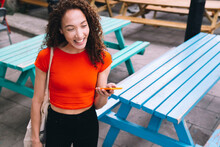Happy Woman Holding Mobile Phone In Front Of Picnic Tables