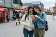 © PR Image Factory - people on vacation in usa. asian woman tourist pointing at fun places to visit as she is checking travel info on the phone with her girl partner on the street at Old Fisherman's Wharf