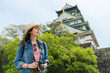 © PR Image Factory - low angle shot portrait of happy asian girl photographer enjoying breeze and looking into distance with magnificent Osaka castle at background in japan