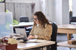 © insta_photos - Young happy professional business woman employee sitting at desk working on laptop in modern corporate office interior. Smiling female worker using computer technology typing browsing web.
