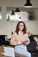 Young happy smiling professional business woman, female company worker or corporate manager holding digital tablet technology posing in modern office working, looking at camera, vertical.