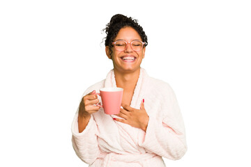 Young brazilian woman wearing a pajama holding a cup isolated laughs out loudly keeping hand on chest.