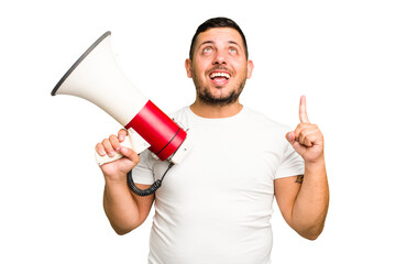 Canvas Print - Young caucasian man holding a megaphone isolated pointing upside with opened mouth.