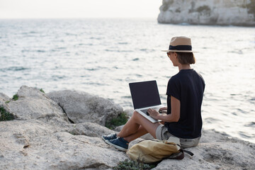 Wall Mural - Young woman using laptop computer working by the sea. Freelance work, vacations, business people, technology, distance studying, e-learning, freelancer lifestyle, meeting online, web call concept.