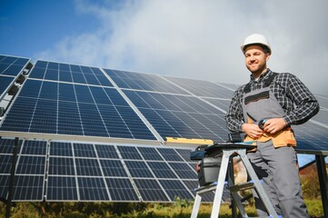 Male worker in uniform outdoors with solar batteries at sunny day.