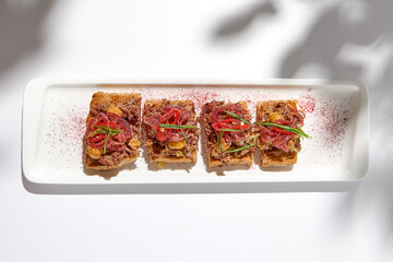 Canvas Print - Aesthetic composition with shredded beef bruschetta on white background with shadows from flowers. Italian bruschetta with shredded beef and mustard on fine dining in summer. Elegant menu concept.