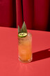 Alcohol tropical  cocktail on red background with shadow. Citrus cocktail in highball glass on coloured background in trendy style. Contemporary concept with alcohol beverage. Bartender cocktail.