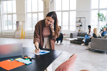 Wall Mural - Woman taking notes during phone call in workplace