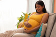 © IndiaPix - Smiling pregnant woman sitting on sofa at home with holding her abdomen