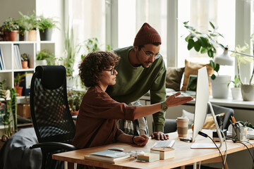 Poster - Young confident female designer or programmer pointing at computer screen while explaining colleague online information