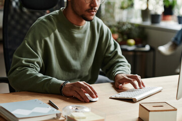 Leinwandbilder - Young man in casualwear clicking mouse and pressing key of computer keyboard while working over new software by workplace