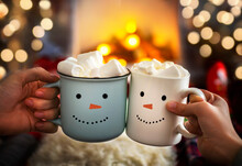 Close-up Of Two Hands With Snowman Face On Cup Of Hot Cocoa With Marshmallows. Mom And Child Relaxing Together On A Cozy Winter Evening By Fireplace. Enjoy Christmas Holidays, Happy Moments At Home.