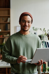 Leinwandbilder - Young confident IT engineer in casualwear looking at camera in office while using laptop and working with online or coded data