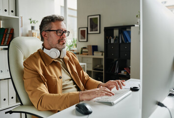 Leinwandbilder - Serious grey haired programmer looking at computer screen while sitting by workplace in front of monitor and decoding data
