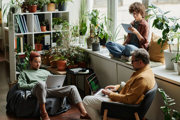 Poster - Three multicultural coworkers in casualwear using mobile gadgets in office while mature IT engineer decoding data on laptop screen