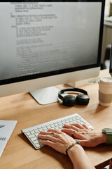 Fototapete - Young businesswoman or programmer pressing keys of computer keyboard while sitting by desk in front of monitor and decoding data