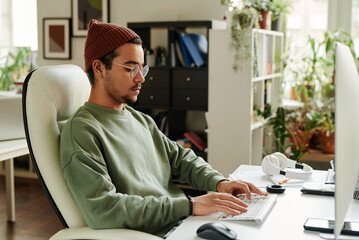 Leinwandbilder - Serious guy in casualwear typing on keyboard while sitting in front of computer monitor and working over new website or software