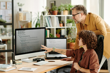 Poster - Young confident programmer pointing at data on computer screen while brainstorming and discussing ways of decoding with colleague