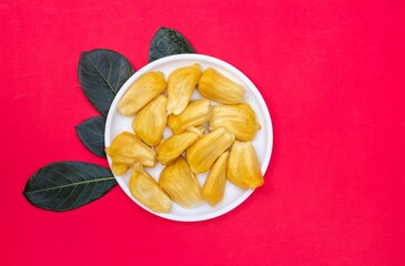 Wall Mural - Top View of Ripe Jackfruit Pieces in a White Plate with Leaves Isolated on Red Background with Copy Space