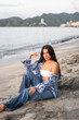 © Hector Pertuz - Latin Woman sitting on the sand next to the shore of the beach