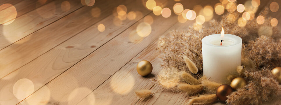 Fototapete - Modern Boho Christmas Advent candle decoration in natural colors. White candle with dried lagurus and pampas grass on wood planks. Golden blurry Bokeh lights. First Advent Sunday. Panorama, Banner.

