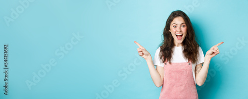 Fototapete Pick your side. Smiling excited woman screaming of joy, pointing fingers sideways at left and right copy space, showing advertisement good deal, standing against blue background