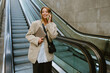 Young woman talking on cellphone while going down escalator outdoors