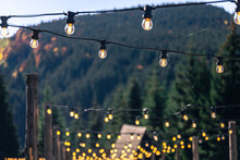 Decorative Light Bulbs On Wooden Poles In A Mountainous Area.
