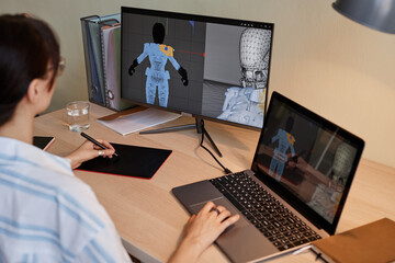 young female designer building digital 3d models for videogame characters at workplace and using pen