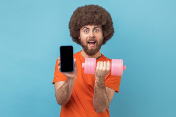 Wall Mural - portrait of shocked man with afro hairstyle wearing orange t-shirt holding dumbbell and smart phone 