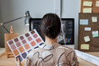 © Seventyfour - Back view of female designer holding color swatches while working with computer at workplace