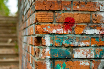 Wall Mural - Close-up of a brick wall with remnants of color drawings and a concrete staircase in soft focus. Backdrop on the topic of a disadvantaged area and abandoned quarters of the city.