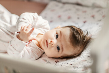 a cute baby girl with blue eyes is looking at the camera while lying in a crib.