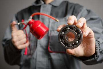 Wall Mural - Car service worker holding in hands a red oil can and car parts on dark background closeup.