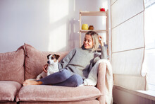 Beautiful Middle-aged Woman With Dog At Home Sitting On Couch