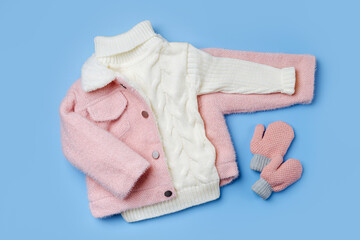 Wall Mural - Kids pink fur jacket with warm sweater on blue background. Stylish childrens outerwear. Winter fashion outfit