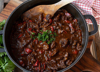 Wall Mural - Beef stew with bell peppers, onions, garlic, tomatoes and herbs in a cooking pot on rustic background