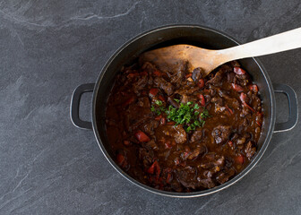 Wall Mural - Pot with fresh cooked spicy beef stew isolated on dark background from above with copy space