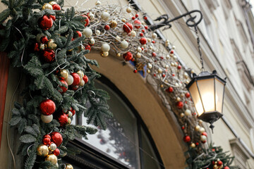 Wall Mural - Stylish christmas red and gold baubles and branches on old door with lantern. Modern christmas decor in city street. Winter holidays in Europe. Merry Christmas and Happy Holidays