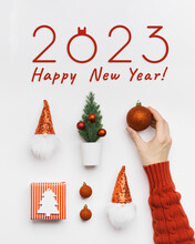 New Year Holiday Flat Lay, Shiny Red Christmas Ball In Woman Hand. Christmas Pattern With Paper Gifts, Dwarfs With Red Shiny Cap, Fir Tree, Text 2023 Happy New Year. Winter Holiday Greetings