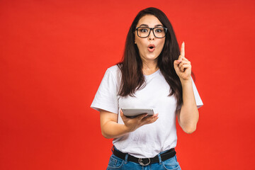 Canvas Print - Portrait of a amazed shocked young brunette business woman using tablet computer isolated over red background.