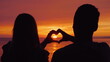 © StockMediaSeller - Silhouettes of a young couple, hands show the shape of the heart against the backdrop of the sunset over the sea