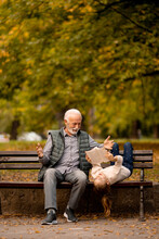 Grandfather Spending Time With His Granddaughter On Bench In Park On Autumn Day
