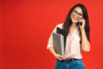 Canvas Print - Pretty young businesswoman in casual holding laptop in the office, isolated over red background. Using mobile phone.