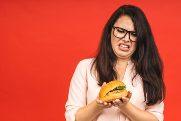 Wall Mural - Young woman isolated on red background studio portrait. Proper nutrition or American classic fast food concept. Mock up copy space. Showing stop or no gesture to burger.