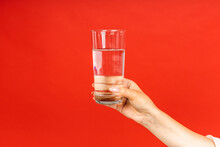 Close-up Photo Of Hand Holding A Glass Of Clean Water Isolated On Red Background.