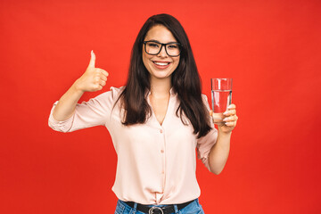 Canvas Print - Young smiling woman holding a glass of water. Isolated studio portrait over red background.