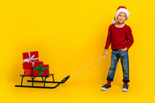 Full Size Photo Of Charming Little Boy Pull Santa Claus Sledge Presents Helper Wear Trendy Red Garment Isolated On Yellow Color Background